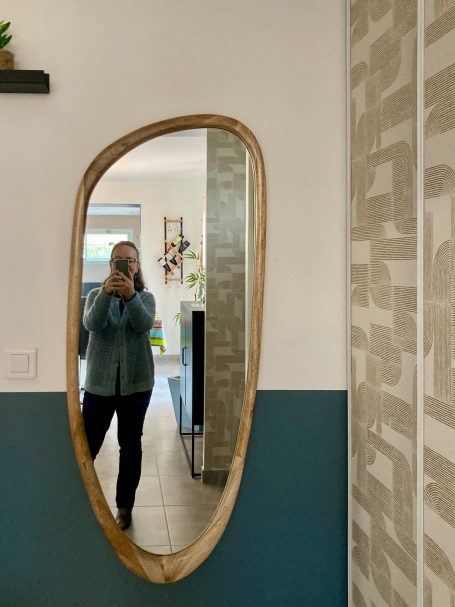 Person se tenant devant un miroir ovale dans un intérieur lumineux et moderne.