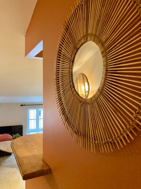 Miroir en rotin accroché sur un mur orange, avec un éclairage doux dans l'arrière-plan.