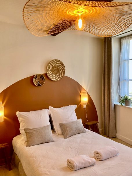 Chambre avec lit double, décoration douce et lampes suspendues en osier.