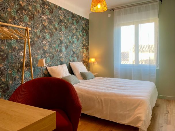 Chambre moderne avec literie blanche, décor floral, et grande fenêtre lumineuse.