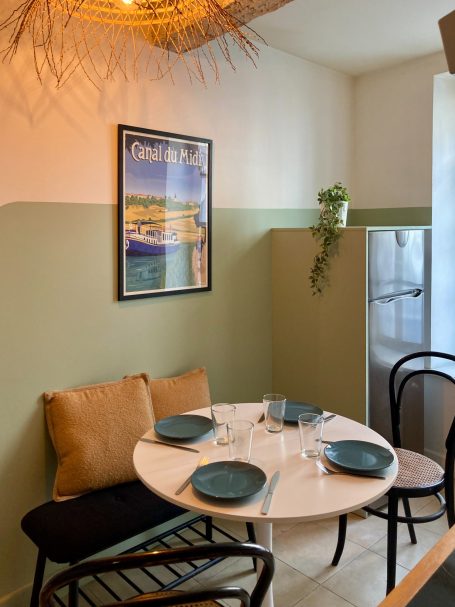 Table ronde avec assiettes, chaises noires et iconographie murale dans une pièce lumineuse.