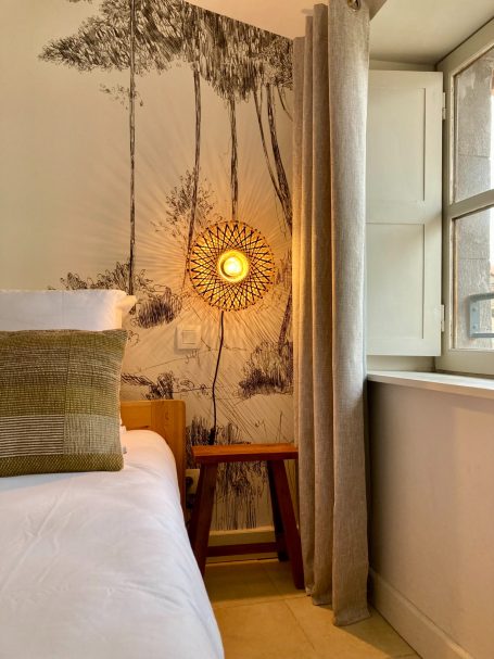 Chambre lumineuse avec un mur décoré d'un motif d'arbres et un éclairage suspendu.