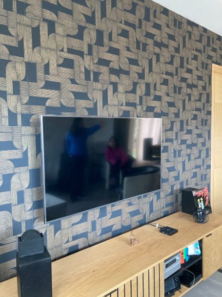Mur en motif beige et bleu avec un téléviseur monté et un meuble en bois en dessous.